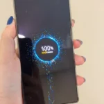 Tela do RedMagic 11 Pro mostrando animação de carregamento rápido 'Max Charge' em 100%, com efeitos de partículas azuis e amarelas, conectado via cabo USB-C vermelho.