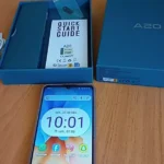 Unboxing do celular Cubot A20 ligado sobre uma mesa, mostrando a tela frontal de 6,75 polegadas e os itens inclusos na caixa.