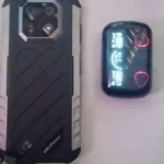 Visão traseira do Ulefone Armor 22 em preto e prata ao lado de um estojo de fones de ouvido, destacando o módulo de câmera dupla.