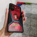Smartphone POCO X7 Pro Edição Especial Marvel Avengers sendo segurado por uma mão, mostrando a traseira vermelha com o reator Ark do Homem de Ferro e o logo dos Vingadores.