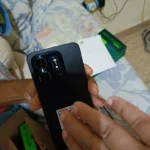 Foto real de um comprador segurando a parte traseira preta do smartphone Infinix Hot 50 Pro durante o unboxing. A imagem mostra o módulo de câmeras e ajuda a avaliar se o infinix hot 50 pro é bom em acabamento.
