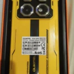 Traseira do smartphone rugged Oukitel WP60 amarelo e preto em ângulo, mostrando o design mech e as quatro câmeras principais dentro da caixa laranja de unboxing. Imagem real de cliente provando que o Oukitel WP60 é bom e robusto.