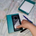 Mão retirando o celular indestrutível Cubot KingKong X Pro da caixa, mostrando o design traseiro militar com mini display digital inteligente de 1.85 polegadas.