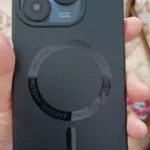 Celular itel a70 é bom para o dia a dia? Foto real do aparelho na mão de um usuário usando capinha preta com anel magnético e conectado ao carregador USB-C.